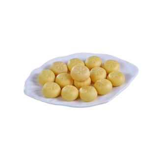 A white plate filled with round, golden-yellow Milk Pedas, each adorned with a delicate flower pattern, showcasing their creamy texture and traditional appeal.