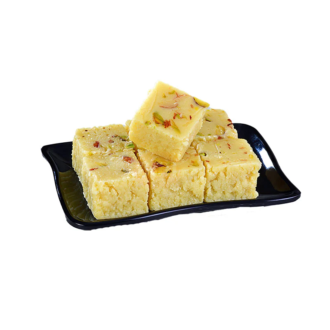 A black plate topped with square pieces of Kalakand Burfi, garnished with pistachios and red and green dried fruits, showcasing its creamy texture and traditional appeal
